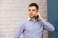 Young smiling man talking mobile phone looking Isolated white brick wall blue shirt Royalty Free Stock Photo