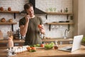 Young smiling man talking on the phone with tomatoe in his habd while cooking breakfast in the kitchen checking recipe in his Royalty Free Stock Photo