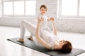 Young smiling mother doing yoga exercise at gym, wearing white sportswear, together with funny little daughter, enjoying Royalty Free Stock Photo