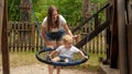 Young smiling mother swinging her cute toddler boy in rope nest swing at park playground Royalty Free Stock Photo