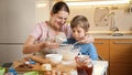 Young smiling mother teaching her son sifting flour with sieve for making biscuit dough. Children cooking with parents Royalty Free Stock Photo