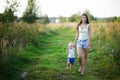 Young smiling mother walks with her little daughter barefoot on a country road at sunset. The nanny walks with the child