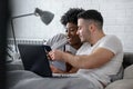 Young smiling multi ethnic couple shopping over internet in the bed in the morning Royalty Free Stock Photo