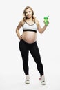 Young smiling pregnant blonde woman in sportswear stands. Healthy motherhood. Full height. Isolated on white background. Vertical Royalty Free Stock Photo