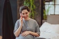 Young smiling pregnant woman touching belly talking on mobile phone with friend while spending time at home Royalty Free Stock Photo