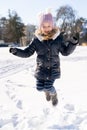Young smiling preschool girl jumping on snow covered field outside in sunny park Royalty Free Stock Photo