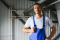 Young smiling professional in overalls and protective helmet standing in front of camera inside large machinebuilding plant Royalty Free Stock Photo