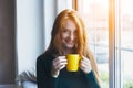 Young smiling red hair woman holding yellow coffee cup, enjoying morning coffee Royalty Free Stock Photo