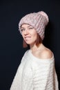 Young smiling red haired girl with bob haircut in pink hat, knitted beige sweater on a white background looking at camera and bit Royalty Free Stock Photo