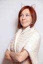 Young smiling red haired girl in a gold rim with ears, knitted beige sweater on a white background looking sideways. Concept