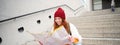 Young smiling redhead girl, tourist sits on stairs outdoors with city paper map, looking for direction, traveller Royalty Free Stock Photo