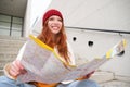 Young smiling redhead girl, tourist sits on stairs outdoors with city paper map, looking for direction, traveller Royalty Free Stock Photo