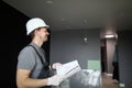 Young smiling repairman standing in empty flat and holding construction plan in hands Royalty Free Stock Photo