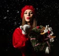 Young smiling beautiful woman dressed in red winter sweater, hat and mittens holding Christmas ornate wreath and sending air kiss