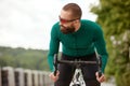 Young smiling sporty man in glasses with beard standing with bike in summer park, cardio workout on bike, city walks Royalty Free Stock Photo