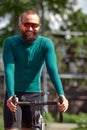 Young smiling sporty man in glasses with beard standing with bike in summer park, cardio workout on bike, city walks Royalty Free Stock Photo