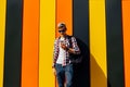 Young smiling stylish man in sunglasses and a cap, uses a mobile phone, leaning against a colorful wall Royalty Free Stock Photo