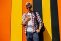 Young smiling stylish man in sunglasses and a cap, uses a mobile phone, leaning against a colorful wall Royalty Free Stock Photo