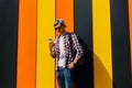 Young smiling stylish man in sunglasses and a cap, uses a mobile phone, leaning against a colorful wall Royalty Free Stock Photo