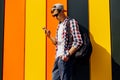 Young smiling stylish man in sunglasses and a cap, uses a mobile phone, leaning against a colorful wall Royalty Free Stock Photo