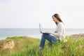 Young smiling successful smart business woman or student in light casual clothes sitting on grass using laptop in field Royalty Free Stock Photo