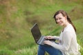 Young smiling successful smart business woman or student in light casual clothes sitting on grass using laptop in field Royalty Free Stock Photo