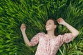 Young smiling tender beautiful woman with closed eyes in light patterned dress lying on grass resting in sunny weather Royalty Free Stock Photo