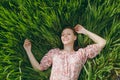 Young smiling tender beautiful woman in light patterned dress lying on grass looking up resting in sunny weather in Royalty Free Stock Photo