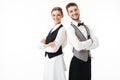 Young smiling waiter and waitress in white shirts and vests sstanding back to back while joyfully looking in camera with