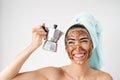 Young smiling woman applying coffee scrub mask on face - Happy girl having healthy skin care spa day at home