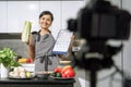 Young smiling woman in an apron holding celery and a comparative table of calorie content of products in her hands and recording Royalty Free Stock Photo