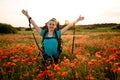 Young smiling woman with backpack stands on poppy field with hands up Royalty Free Stock Photo