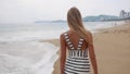 Young smiling woman in black and white dresses walking alone on a tropical beach and looking at camera over background