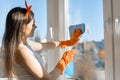 Young smiling woman cleaning window, with spray window cleaner and rag in rubber gloves, spring cleaning at home Royalty Free Stock Photo