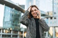 Young smiling woman in coat with coffee cup using mobile phone in evening city street