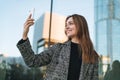 Young smiling woman in coat taling selfie on mobile phone in evening city street