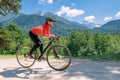 A young smiling woman on a cyclocross bike rides against the background of a green forest on a sunlit road