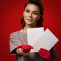 Young smiling woman doctor therapist in protective latex gloves holding two paper sheets blanks, pointing and looking at