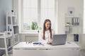 Smiling woman doctor sitting in medical clinic office with laptop and communicating online with somebody Royalty Free Stock Photo