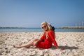 Young smiling woman in elegant red dress sits on on the beach Royalty Free Stock Photo