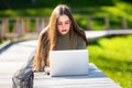 Young elegant woman in eyeglasses lying on bench in park and working on laptop on a sunny and windy day Royalty Free Stock Photo