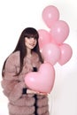 Young smiling woman in fashion fur coat holding pink heart over