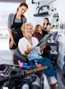 Young woman hairdresser in hair salon helping to senior woman ch