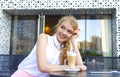 Young smiling woman having coffee break sitting at cafe and drinking latte through straw. Fashionable blond european girl enjoying Royalty Free Stock Photo