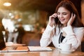 Young smiling woman having pleasant phone conversation working outside office during lunch break drinking hot coffee in cafe Royalty Free Stock Photo