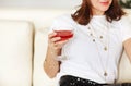 Young smiling woman holding cocktail glass in hand with red alcohol drink sitting on sofa at home Royalty Free Stock Photo