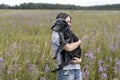 Young smiling woman holding gray fluffy senior dog in hands on meadow with flowers of fireweed or great willowherb, pet love Royalty Free Stock Photo