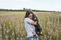 Young smiling woman holding gray fluffy senior dog in hands on meadow with flowers of fireweed or great willowherb, pet love Royalty Free Stock Photo