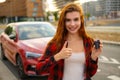 Young smiling woman holding in hand car key sand shows thumb up like gesture standing in the street