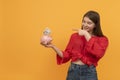 Young smiling woman holds piggy bank and points with finger at it. Concepts of saving money and investments Royalty Free Stock Photo